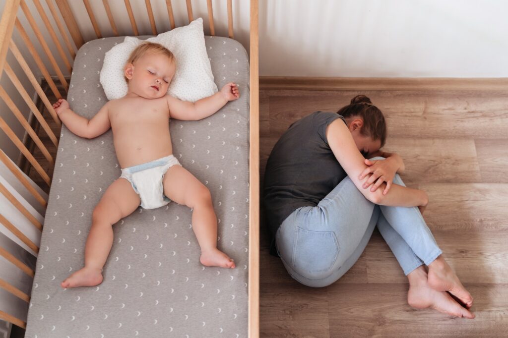 Upper view of baby napping in bed next to mother lying on floor suffering postnatal depression